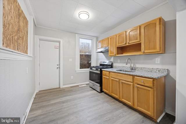 kitchen with under cabinet range hood, light wood-type flooring, stainless steel range with gas cooktop, and a sink