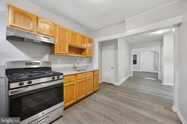 kitchen with light wood-style flooring, under cabinet range hood, a sink, light stone countertops, and stainless steel gas range