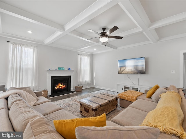 living area with baseboards, beamed ceiling, a warm lit fireplace, wood finished floors, and coffered ceiling