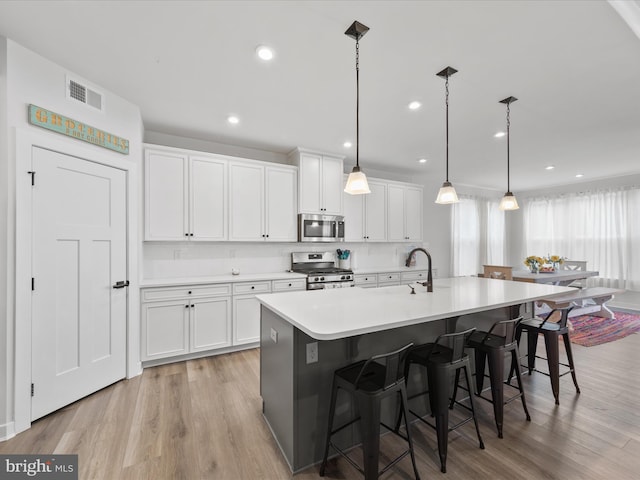 kitchen with a kitchen bar, white cabinets, light wood-style floors, and stainless steel appliances