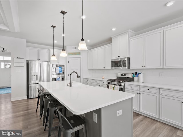 kitchen featuring decorative backsplash, light wood-style flooring, appliances with stainless steel finishes, and an island with sink