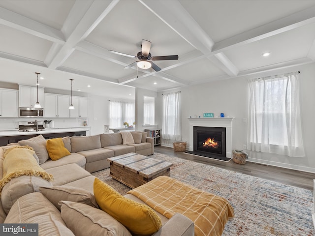 living area with baseboards, coffered ceiling, a lit fireplace, and wood finished floors