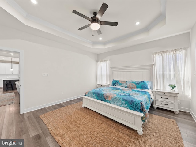 bedroom featuring a tray ceiling, wood finished floors, recessed lighting, crown molding, and baseboards