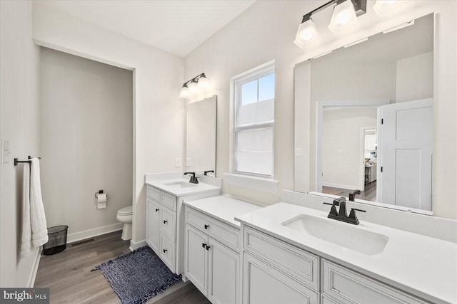 full bathroom with a sink, toilet, two vanities, and wood finished floors