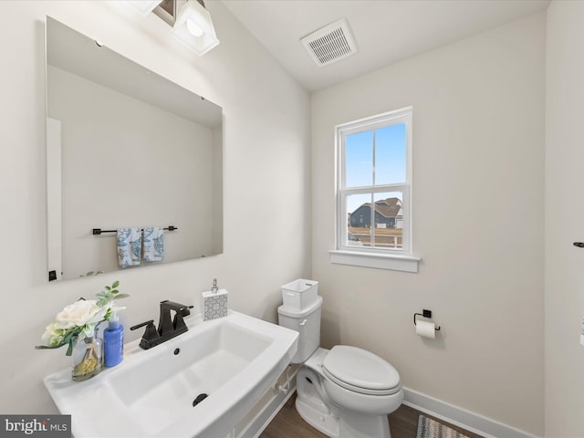 half bathroom with visible vents, toilet, a sink, wood finished floors, and baseboards