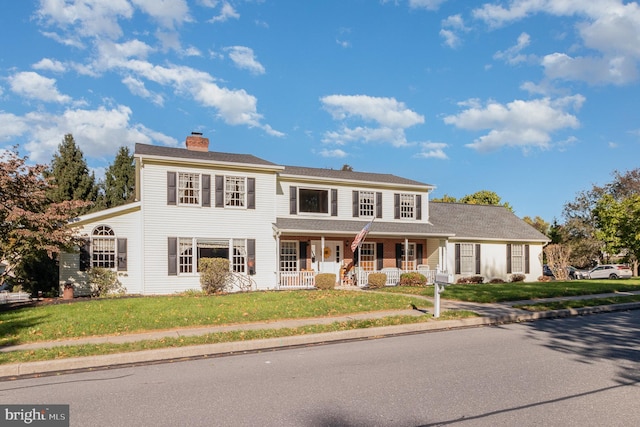 colonial-style house featuring covered porch, a chimney, and a front lawn