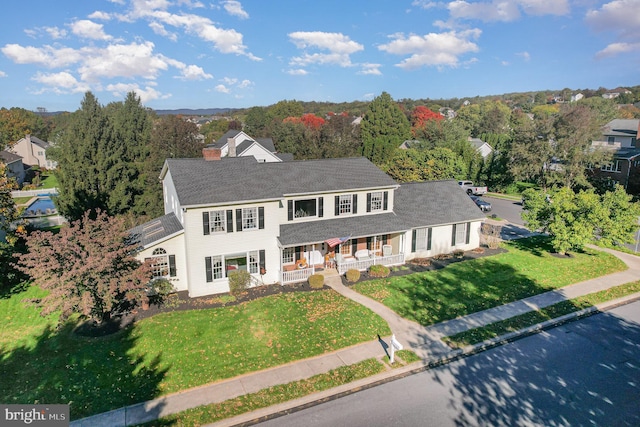 view of front of home with covered porch, a chimney, and a front lawn