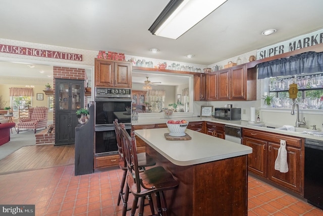 kitchen featuring light tile patterned floors, light countertops, a sink, black appliances, and a kitchen breakfast bar