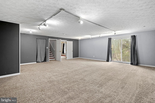 below grade area featuring stairway, carpet, baseboards, track lighting, and a textured ceiling