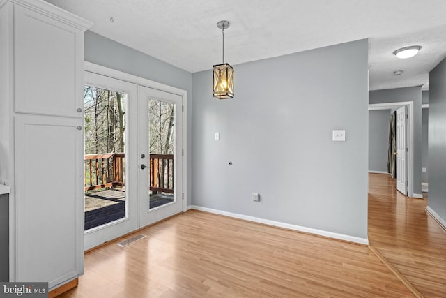 unfurnished dining area featuring visible vents, a textured ceiling, french doors, light wood-style floors, and baseboards