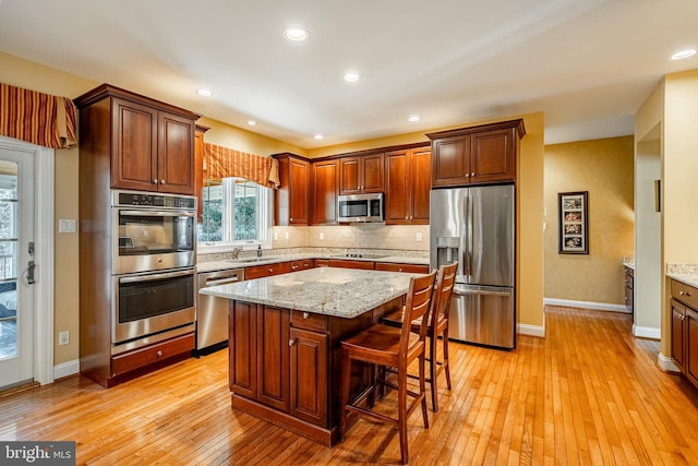 kitchen with a kitchen bar, light wood-style flooring, a sink, stainless steel appliances, and decorative backsplash