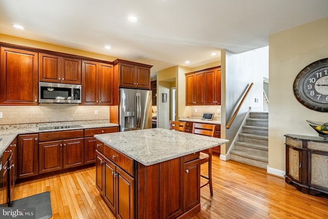 kitchen featuring a kitchen bar, backsplash, light wood-style floors, appliances with stainless steel finishes, and light stone countertops