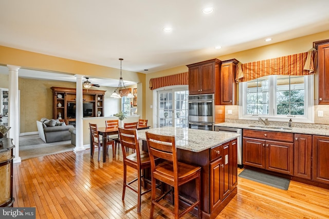 kitchen with tasteful backsplash, decorative columns, light wood-style flooring, stainless steel appliances, and a sink