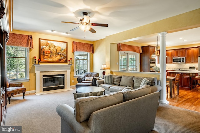 living room with baseboards, ceiling fan, carpet floors, decorative columns, and a premium fireplace