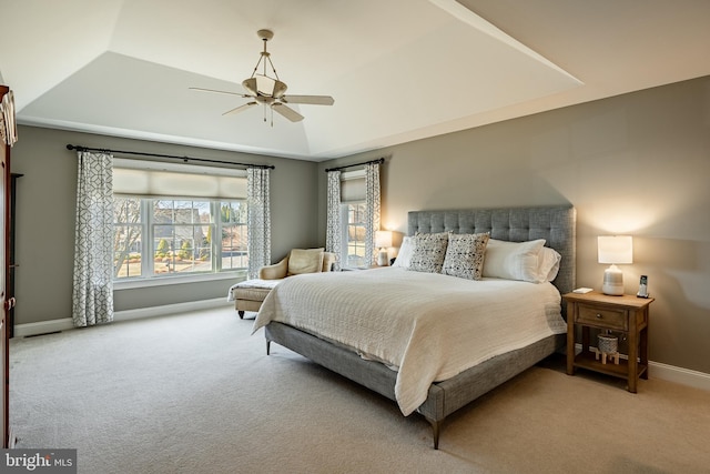 carpeted bedroom with a ceiling fan, a raised ceiling, and baseboards