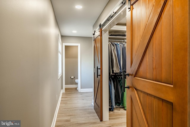 corridor featuring recessed lighting, light wood-style flooring, baseboards, and a barn door