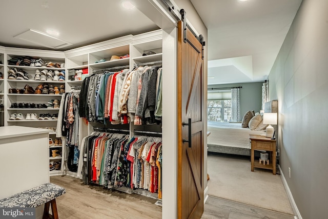 spacious closet featuring attic access, a barn door, and wood finished floors