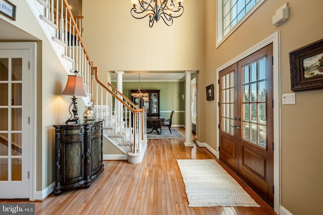 entryway with a notable chandelier, hardwood / wood-style floors, stairs, and ornate columns