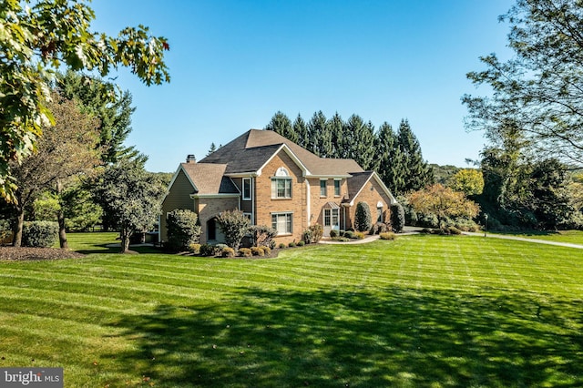 view of front of property with brick siding, a chimney, and a front lawn