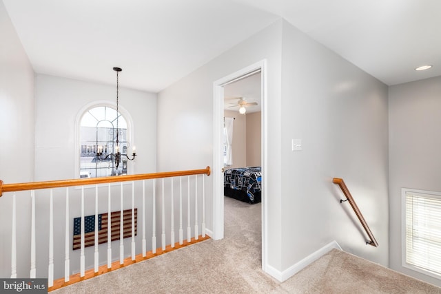 hall featuring carpet, a notable chandelier, plenty of natural light, and an upstairs landing