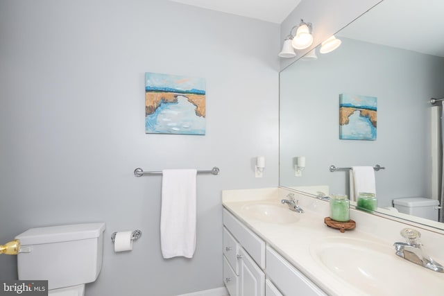 bathroom featuring a sink, baseboards, toilet, and double vanity