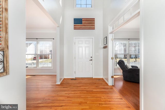 foyer entrance featuring light wood-type flooring, baseboards, a high ceiling, and ornamental molding