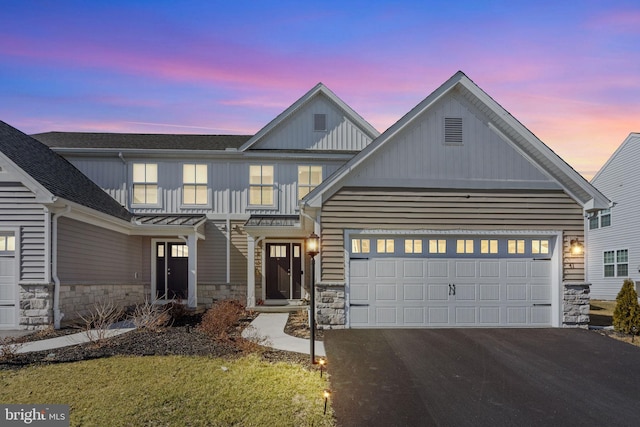 view of front of property with stone siding, an attached garage, board and batten siding, and driveway