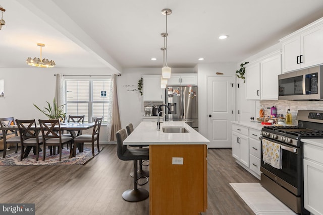 kitchen with dark wood-type flooring, an island with sink, backsplash, and stainless steel appliances