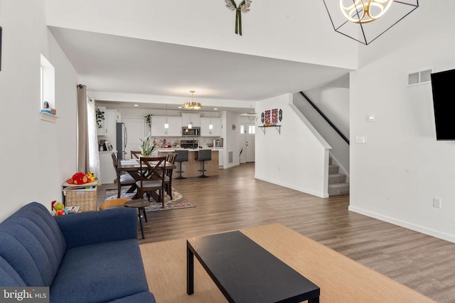 living area featuring stairway, a notable chandelier, light wood-style floors, and visible vents