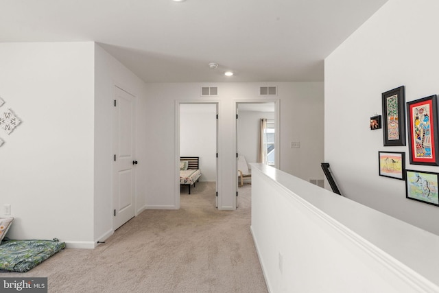 hallway with visible vents, an upstairs landing, and light colored carpet