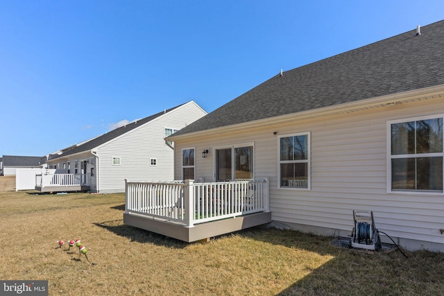 back of property featuring a wooden deck, a yard, and roof with shingles