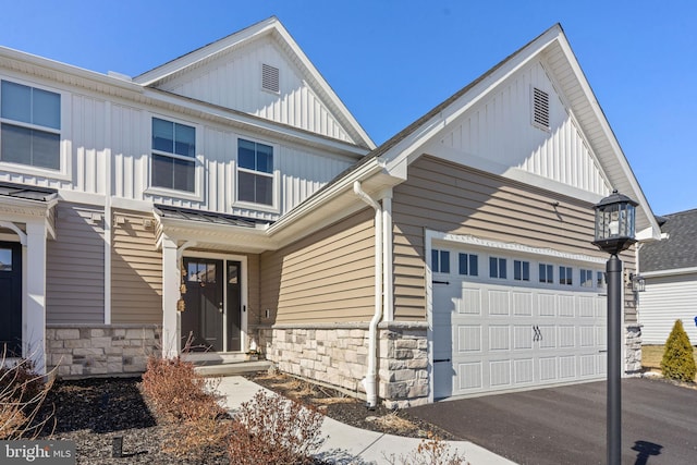 view of front of house featuring stone siding, an attached garage, board and batten siding, and driveway