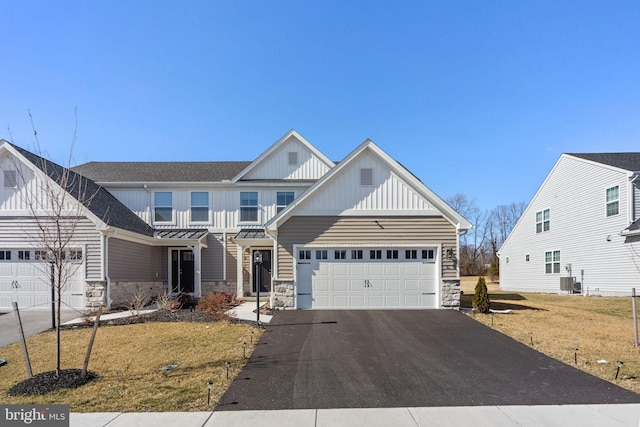 view of front facade featuring aphalt driveway, stone siding, board and batten siding, a front yard, and a garage