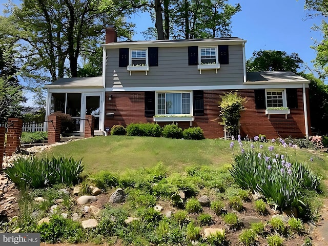 view of front of home with brick siding, a front lawn, a chimney, and a sunroom