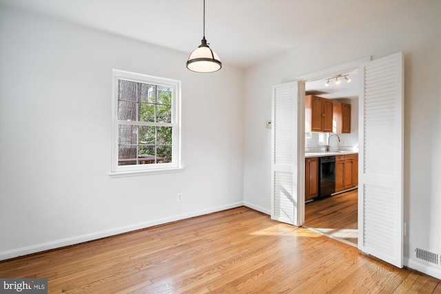 unfurnished dining area with visible vents, light wood-type flooring, baseboards, and a sink