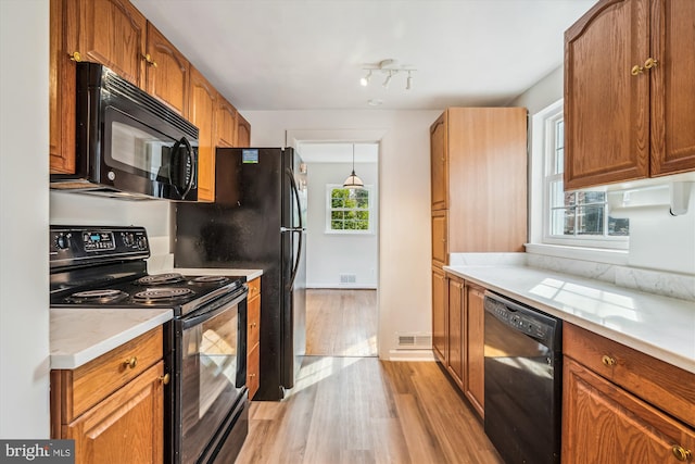 kitchen featuring light wood finished floors, visible vents, decorative light fixtures, brown cabinets, and black appliances