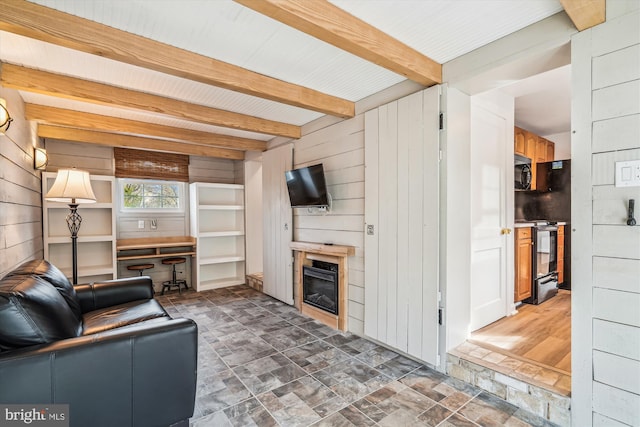 living room featuring a glass covered fireplace, beamed ceiling, wood walls, and stone finish flooring