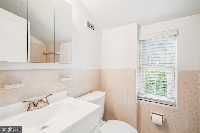 bathroom with a wainscoted wall, visible vents, vaulted ceiling, tile walls, and toilet