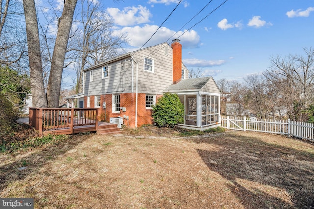 back of house with a deck, a fenced backyard, a sunroom, brick siding, and a chimney