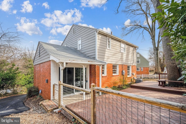 exterior space with brick siding, a wooden deck, and fence