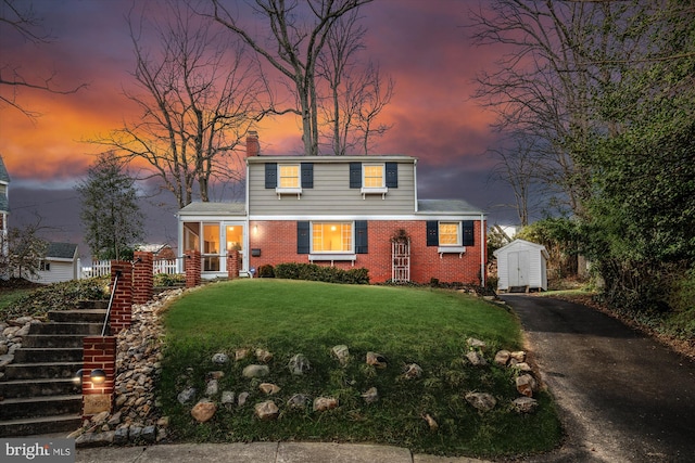 view of front of property featuring a storage unit, an outdoor structure, a front yard, brick siding, and a chimney