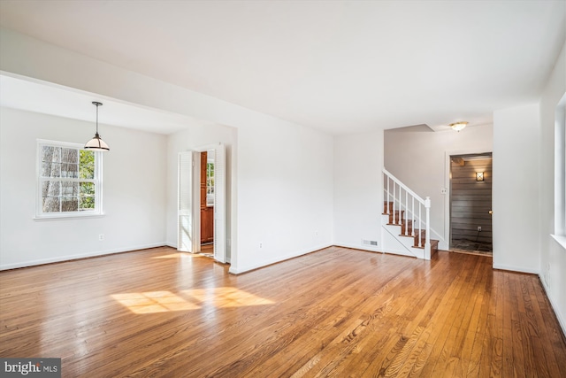 empty room featuring visible vents, light wood-style flooring, stairs, and baseboards