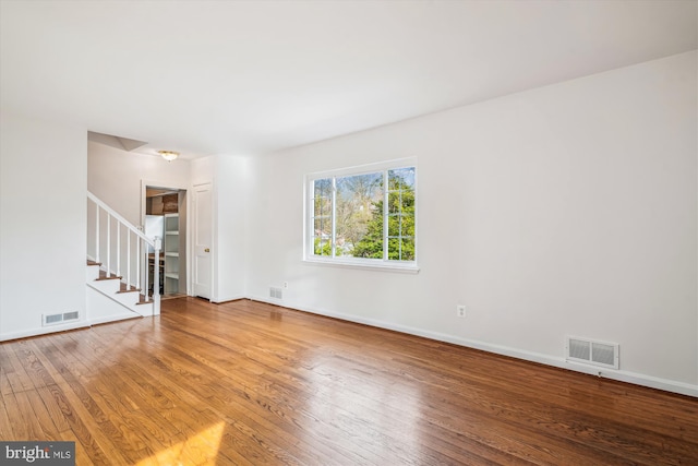 spare room with visible vents, wood-type flooring, baseboards, and stairway