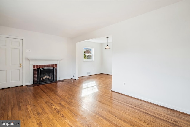 unfurnished living room with a fireplace, visible vents, wood finished floors, and baseboards