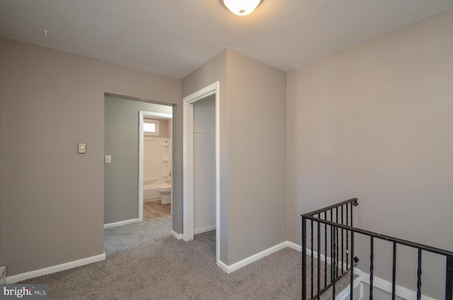 hallway with carpet, baseboards, and an upstairs landing