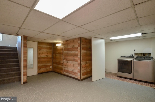 finished basement with stairway, washing machine and dryer, a paneled ceiling, and wooden walls