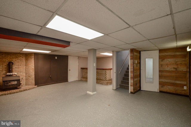 finished basement featuring a wood stove, a drop ceiling, and stairway