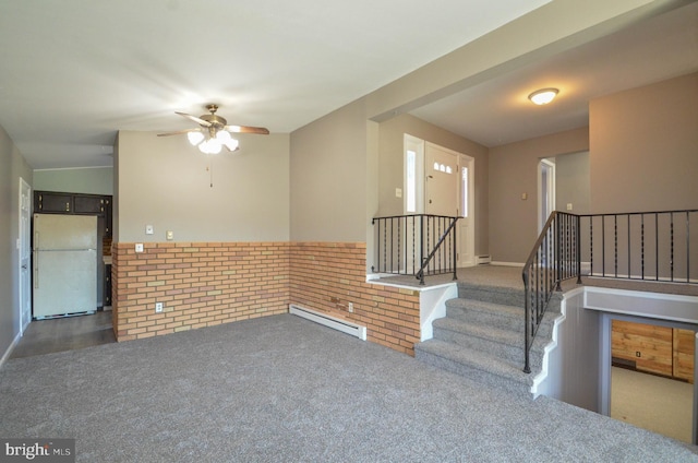 carpeted spare room with a baseboard heating unit, ceiling fan, wainscoting, and stairs