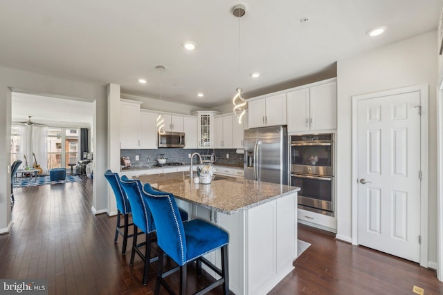 kitchen featuring light stone counters, tasteful backsplash, stainless steel appliances, glass insert cabinets, and dark wood-style flooring