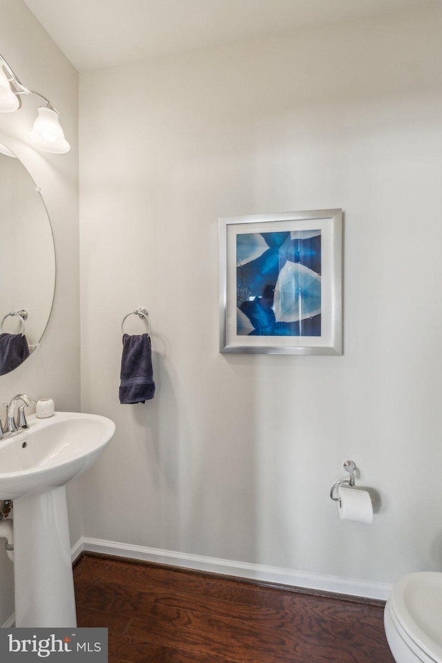 bathroom featuring toilet, wood finished floors, baseboards, and a sink